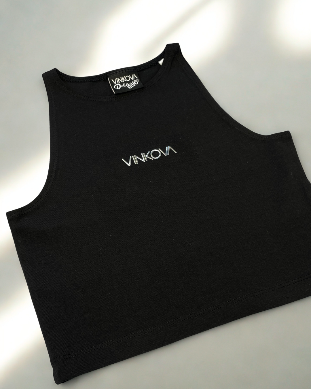 Schwarzes Vinkova Neckholder-Top, Detail von hohem Ausschnitt und Brustlogo.