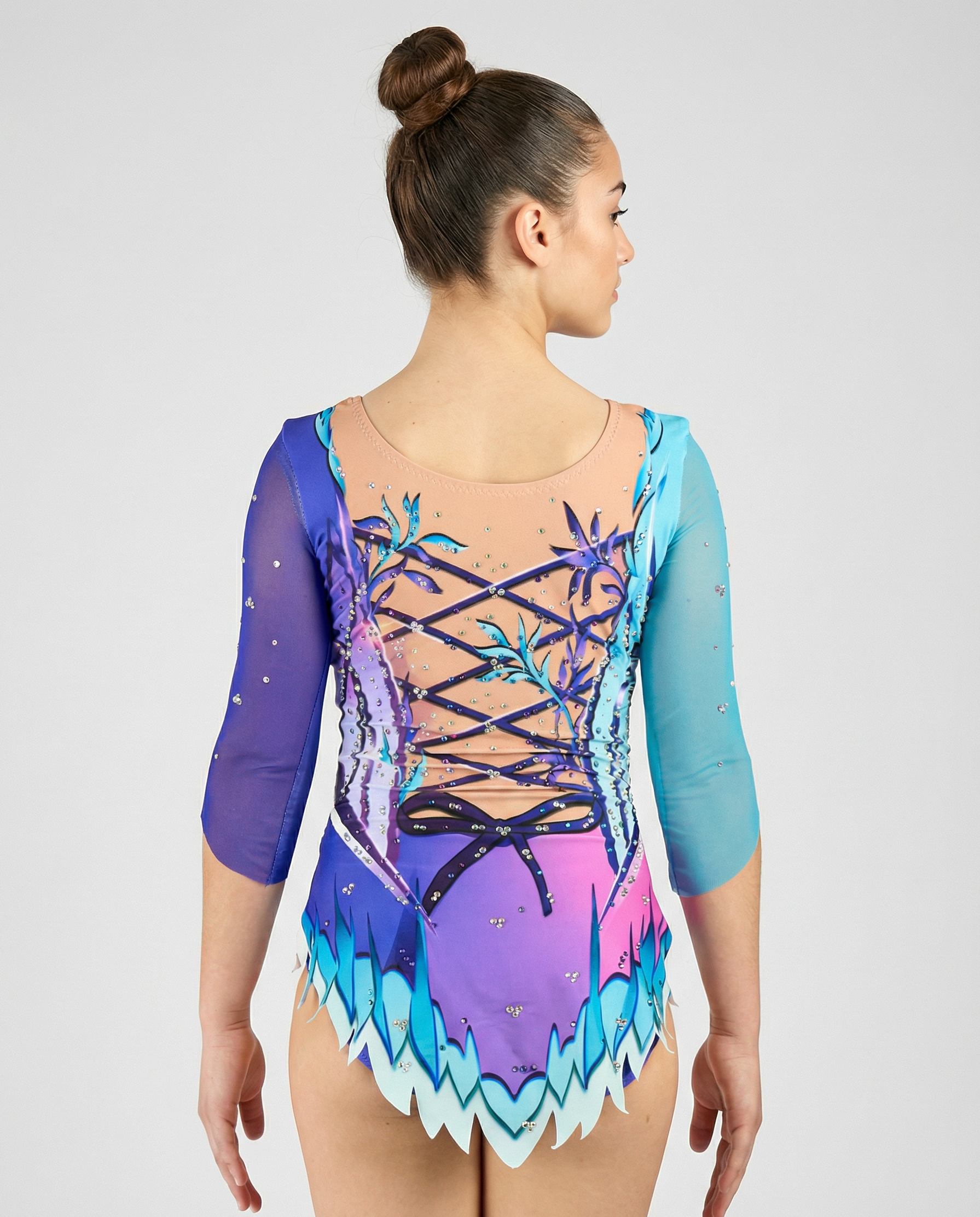 Maillot de gimnasia rítmica en degradado rosa-morado con mangas turquesa, pedrería y motivos florales creando un estilo delicado y luminoso.
Maillot rítmico turquesa y morado con degradados, pedrería y detalles florales que aportan un diseño elegante y fantasioso.
Espalda de maillot rítmico en tonos turquesa y morado con transparencias, pedrería y diseño floral con lazos impresos en un estilo mágico.