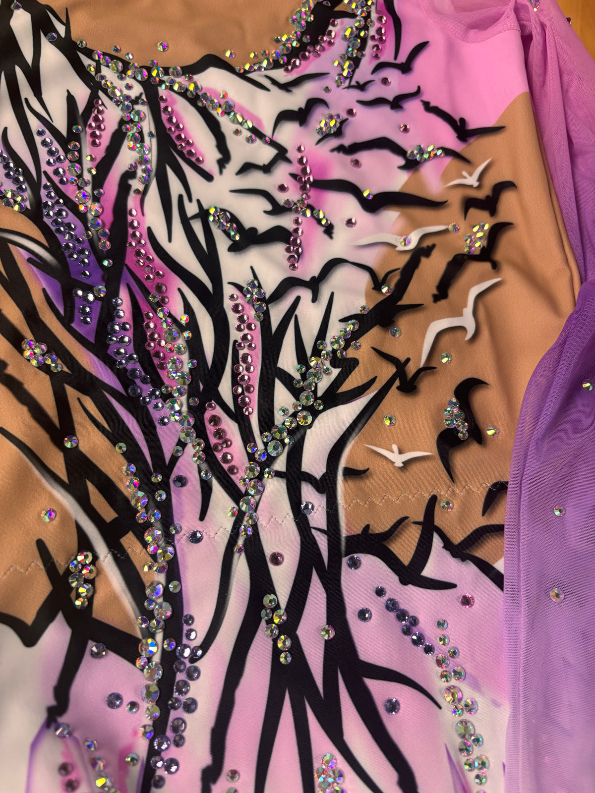 Nahaufnahme von Reihen dunkler, pinker und irisierender Steine auf schwarzen Zweigen, weißen und violetten Flächen mit Vögeln.