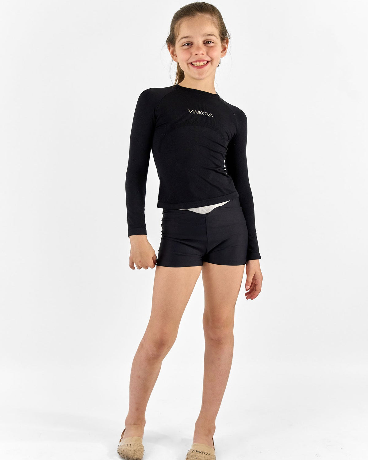 Turnerin in schwarzem Vinkova RSG-Thermoshirt mit langen Ärmeln und schwarzen Shorts.
