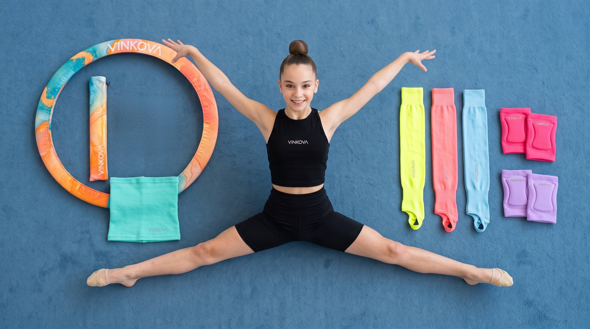 Gymnastin im Spagat neben Reifenhülle, Hüftwärmer, Beinstulpen und VINKOVA Knieschonern vor blauem Hintergrund.