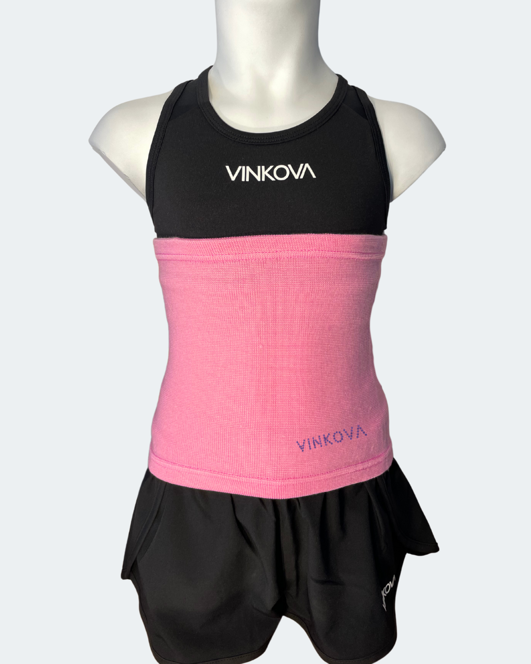Vinkova Nierenwärmer in rosa an einer Schaufensterpuppe mit schwarzem Outfit.